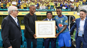 Vini Jr, atacante da Seleção Brasileira, segurando o certificado de ancestralidade, ao lado do pai (foto: André Frutuôso)