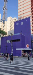 Vemos um balcão de pedidos do Burger King. Apesar de nas telas de televisão penduradas no alto exibirem o cardápio como sempre, as paredes, o balcão e o piso estão roxos, cor oficial do Nubank